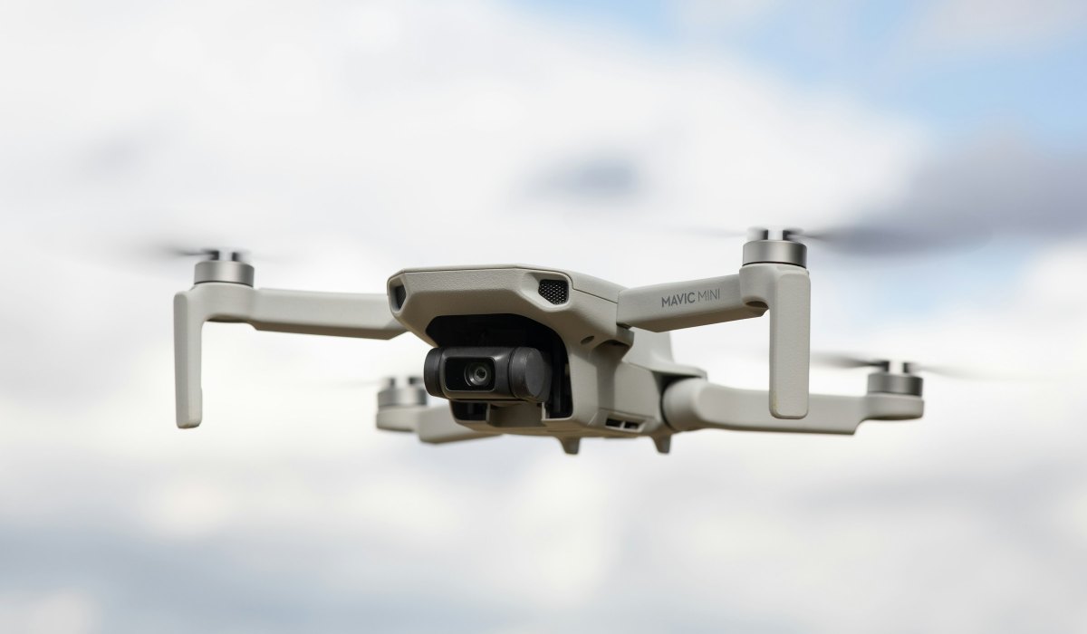 Compact white sub-250 g camera drone in flight against a pale sky, the weight class the DJI Neo 3 stays in